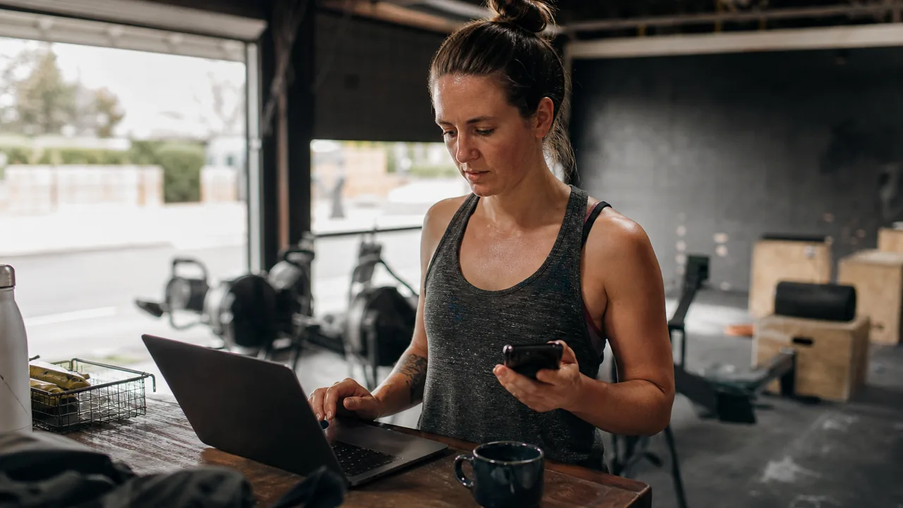 Gym owner at the front desk of a functional fitness box checking messages on her phone before morning classes